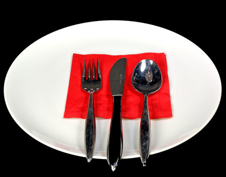 A white plate and utensils on a black background.