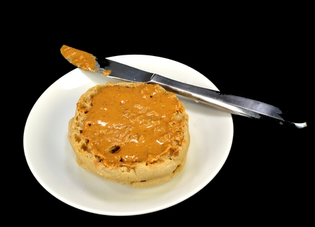English muffin with peanut butter and a knife on a black background.の写真素材