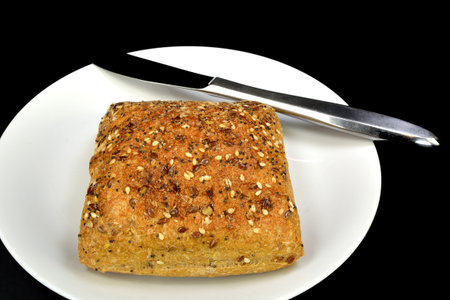 Multigrain Ciabatta roll with a knife on a black background.