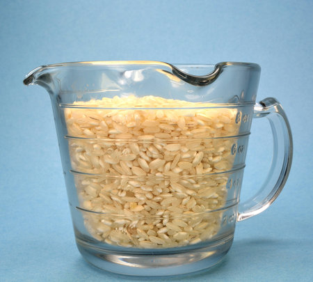 Measuring cup filled with brown rice on a blue background.の写真素材