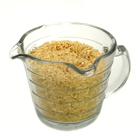 Measuring cup filled with brown rice on a white background の写真素材