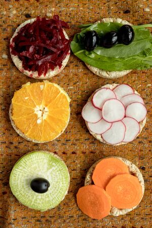 vegetarian sandwiches. on grain loaves lie. repeating the shape of the circle radishes, green radishes, carrots, beets cut into strips, olives, sorrel and orange. it harmonizes with a warm textured dark orange backgroundの写真素材