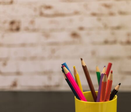 a few colored pencils. pencils of different colors. colored pencils stand in a cup. The background is a brick wall painted. glass of yellow. pencils for children.の写真素材