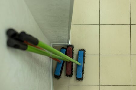 mops of different colors stand near the wall in a clean room. brushes for sweeping the floor stand near the wall. three brushes for the floor. clean indoors. There is no dirt in the building.の写真素材