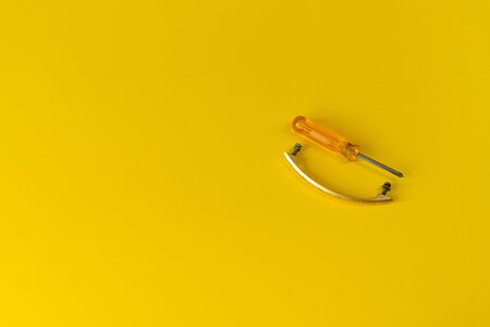 screwdriver with orange handle and a cabinet handle with bolts. handle for a closet with screws and a screwdriver nearby. yellow backgroundの写真素材
