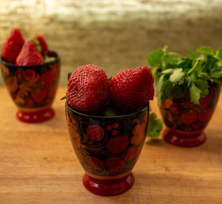 a composition of three painted cups with berries in the drawing and strawberries inside. in the third glass of greens. they stand on a wooden cutting Board. light grey backgroundの写真素材