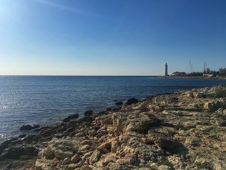 the black sea coast in an unusual place, with a rocky grass surface on a bright Sunny day. a lighthouse is visible in the distanceの写真素材