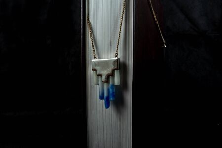 against a dark background stands a thick, tall book with tightly compressed pages. on it hangs a chain with a pendant made of marble in two colors. bijouterieの写真素材