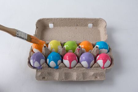eggs painted with different colors are in an egg box on a white background, brush on the left in the plate with paintingsの写真素材