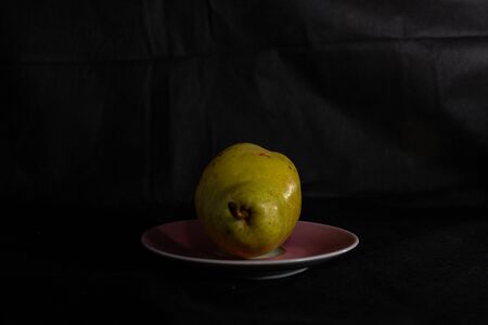 a juicy pear is lying on a pastel pink saucer on a dark backgroundの写真素材