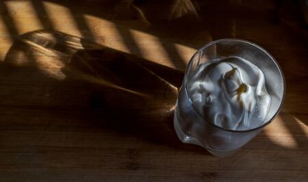a transparent glass with thick sour cream, yogurt, sweet cream stands on a wooden Board, warmly illuminated by a beautiful warm lightの写真素材