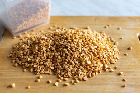 yellow dry peas are scattered on a wooden Board. next to it is a container that also contains peas. table and wooden Board in the kitchen. raw.の写真素材