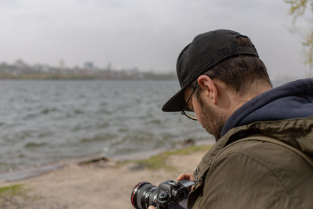 attractive guy in a cap and with a camera. male photographer. the riverbank overlooking the city....
