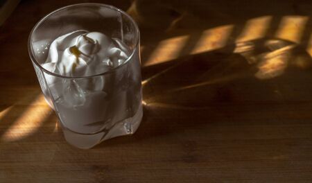 a transparent glass with thick sour cream, yogurt, sweet cream stands on a wooden Board, warmly illuminated by a beautiful warm lightの写真素材