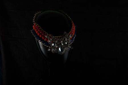 A necklace made by hand in an unusual way is presented of a portrait mannequin woman. On a dark background and highlighted at the back, the necklace glitters. Reflections. Not precious stones or metalの写真素材