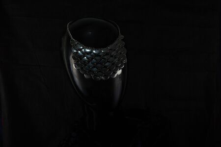 A necklace made by hand in an unusual way is presented of a portrait mannequin woman. On a dark background and highlighted at the back, the necklace glitters. Reflections. Not precious stones or metalの写真素材