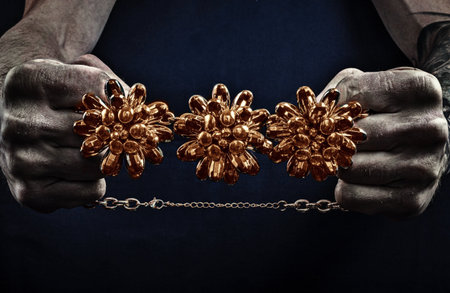 strong male working hands hold contrasting bright jewelry on a dark background. tattoos on the arms....