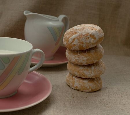 milk in a tea cup with pastel strips stands on a light gray background. near the milk container. Both on a pink plates. gingerbread or cookies are stacked on top of each other.の写真素材