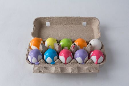 eggs painted with different colors are in an egg box on a white backgroundの写真素材