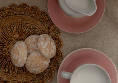 milk in a tea cup with pastel strips stands on a light gray background. near the milk container. Both on a pink plates. gingerbread or cookies are stacked on top of each other.の写真素材