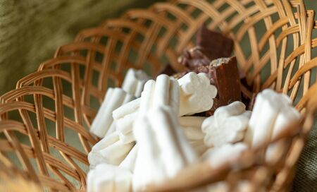 marshmallows and chocolate lie in the same wicker basket. marshmallows elongated and airy. chocolate with waffles and nuts. lovely sweets to a cup of coffee or tea. High quality photoの写真素材
