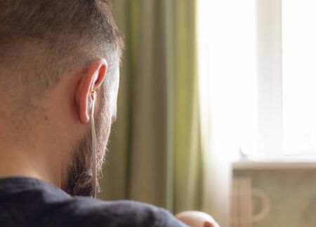 a man sits in headphones in front of the window, from where the bright daylight is pouring. he listens intently. short haircut and beard. . High quality photoの写真素材