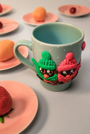 The original mug with decorative figurines made with their own hands. Figures on the cup are fashioned hand made from colored clay. Fruits and berries on a plates around. High quality photoの写真素材