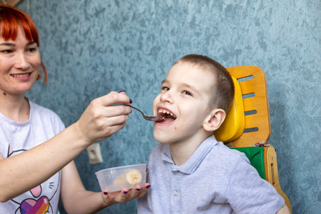 Boy with cerebral palsy and his mom in the conditions of his apartment. Boy reacts vividly to everything that happens around him and shows it with his personality. High quality photoの写真素材