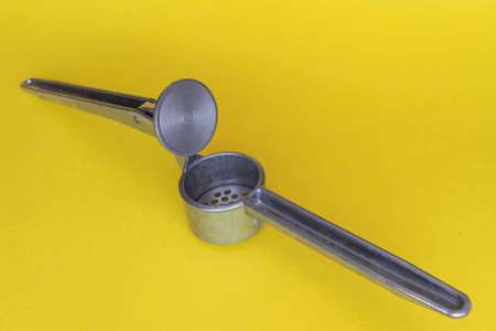 a steel hand press for chopping garlic lies on a bright contrasting yellow background. High quality photoの写真素材