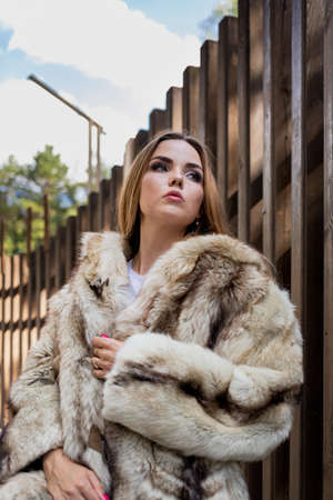 a beautiful girl with long hair and expressive eyes poses in a fur coat in a Park. High quality photoの写真素材