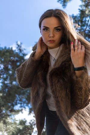 a beautiful girl with long hair and expressive eyes poses in a fur coat in a Park. High quality photoの写真素材