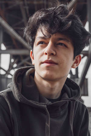 a young guy of Eastern appearance with black hair and a handsome expressive face poses in a Park against the background of trees and architecture. High quality photoの写真素材