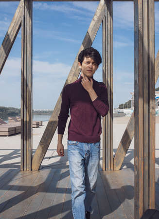 a young guy of Eastern appearance with black hair and a handsome expressive face poses in a Park against the background of trees and architecture. High quality photoの写真素材