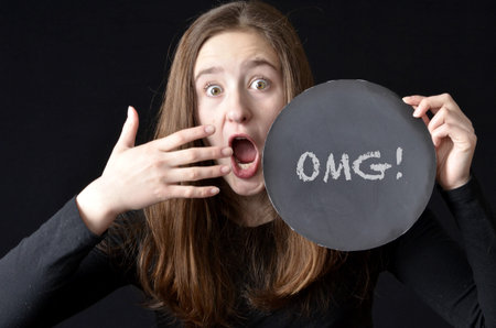 Teenaged girl with a surprised expression holding an OMG! sign wearing black shirt on black...