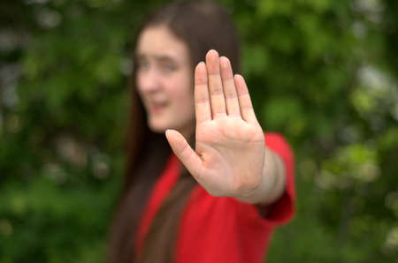 Teen girl with outstretched hand wearing red shirt on green background with only the hand in focus.の写真素材