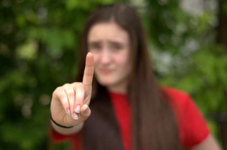 Teen girl with outstretched hand with pointer extended wearing red shirt on green background with only the hand in focus.の写真素材
