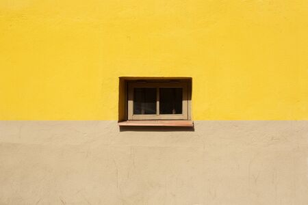 Colorful wall fragment with small window in the middle background. Yellow and beige house wall on sunny summer day close up.の写真素材