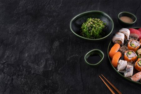 Assorted sushi set served on dark stone slate background. Seaweed wakame salad, seafood, various maki rolls, sashimi and nigiri with caviar, prawn, salmon, eel, mackerel and tuna. Copy space for textの写真素材