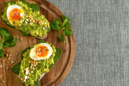 Close up of an avocado toasts with soft boiled egg, herbs, spinach, salad and nuts on a round wooden...