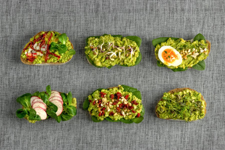 Variety of open bruschetta sandwiches with avocado, soft boiled egg, radish, spinach, herbs and nuts on a gray background.の写真素材