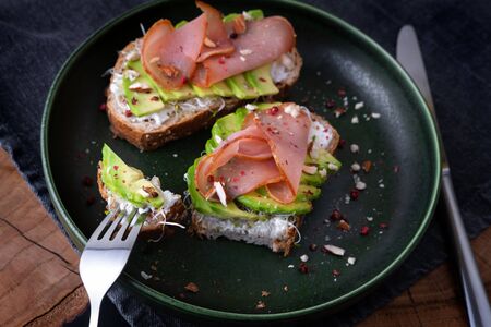 Avocado sandwiches close up on green plate with fork and knife on wooden table with gray denim table cloth.の写真素材