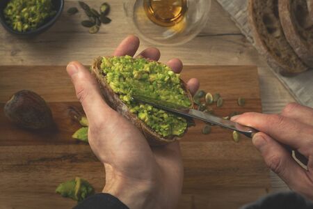Close up of a chef hands making avocado sandwich on a wooden table. Toast with hummus. Man making breakfast in the kitchen.の写真素材
