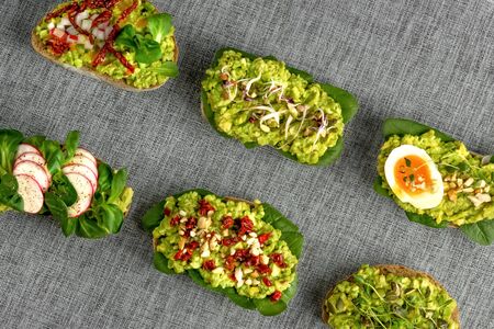 Variety of open bruschetta sandwiches with avocado, soft boiled egg, radish, spinach, herbs and nuts on a gray background.の写真素材