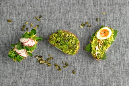 Avocado toasts. Variety of open bruschetta sandwiches with avocado, soft boiled egg, radish, spinach, herbs and nuts on a gray background.の写真素材