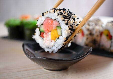 Close up of sushi maki roll with salmon, snow crab and vegetables in chopsticks with soy sauce.の写真素材