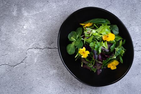 Tasty healthy vegan salad bowl with greens, vegetables and flowers on gray stone background. Healthy food. Top view with copy spaceの写真素材