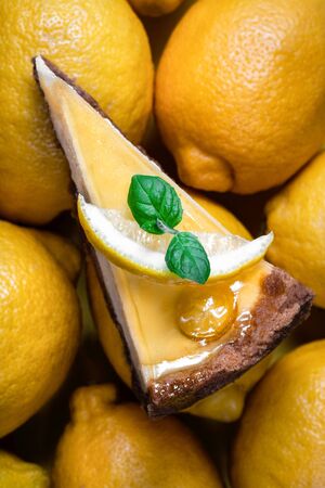 Lemon cheesecake slice with fresh mint leaf and yellow ripe lemons on the background. Beautiful, delicious cake on creative background. Dessert close up, top viewの写真素材