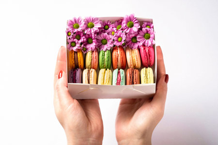 Woman holding in hands gift box with colorful french macaroons with flowers on white background. Valentines Day (February 14), Mother's day, Birthday or Woman's day (8 March) concept. Copy spaceの写真素材