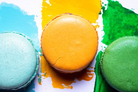 Bright colorful macaroons background. Blue, yellow and green macaroons on painted backdrop. Variety of french almond macaron cookies. Dessert, sugar, gift or bakery concept. Macro shot, top view, close upの写真素材