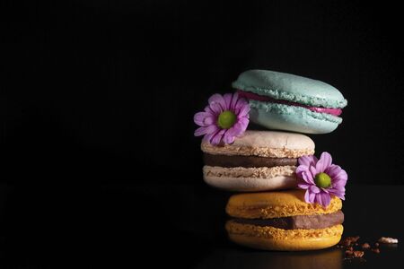 Colorful macaroons with flowers on dark black background. Variety of french almond macaron cookies in pile.Dessert, sugar, bakery creative concept. Macro shot, side view, close up, copy space. Low keyの写真素材